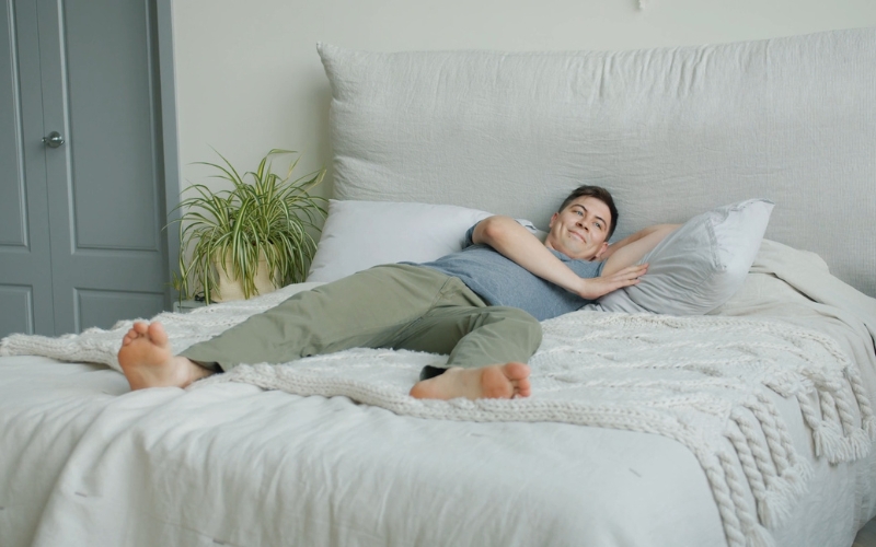 Muškarac koji opušteno leži na krevetu u svetloj spavaćoj sobi.