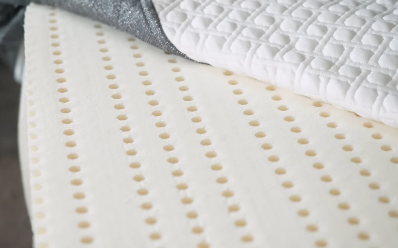 Detalj dušeka koji prikazuje belu štepanu navlaku sa geometrijskim šarama i perforiranu penu sa pravilnim ventilacionim otvorima.