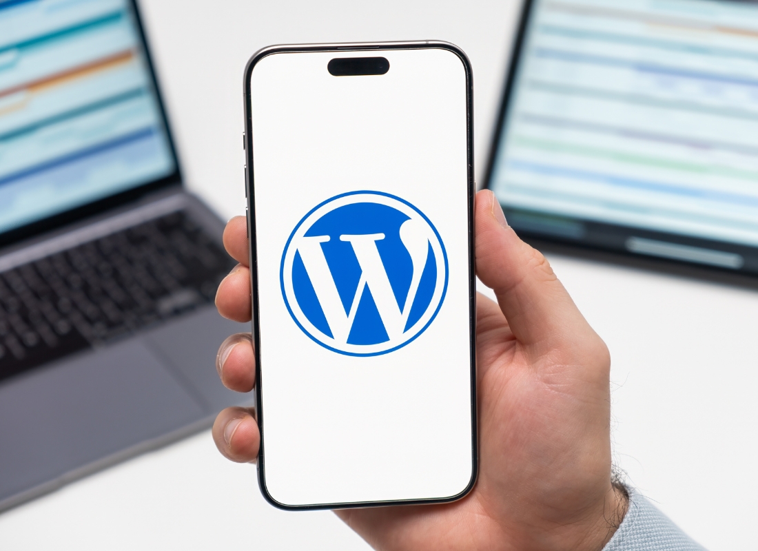 momak drži telefon sa logom wordpressa u ruci u pozadini laptop i tablet