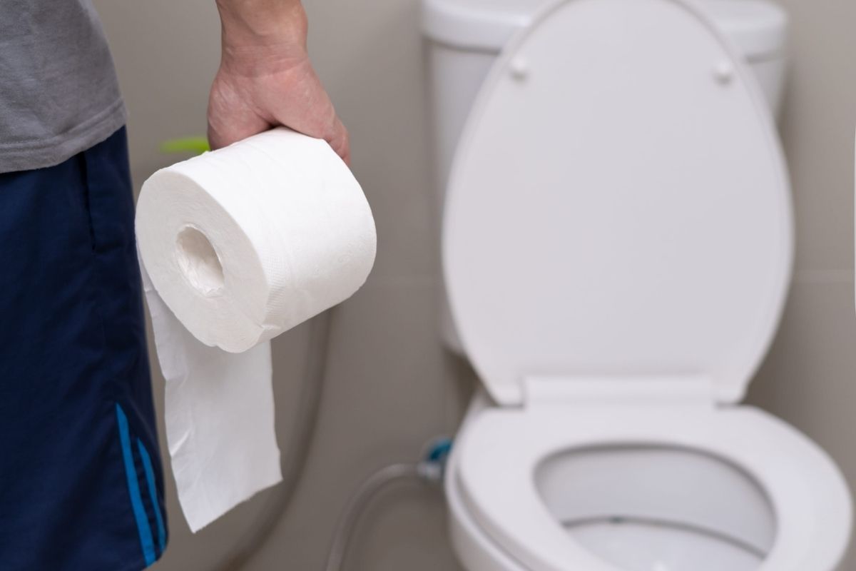 osoba drži toalet papir u ruci ispred wc šolje
